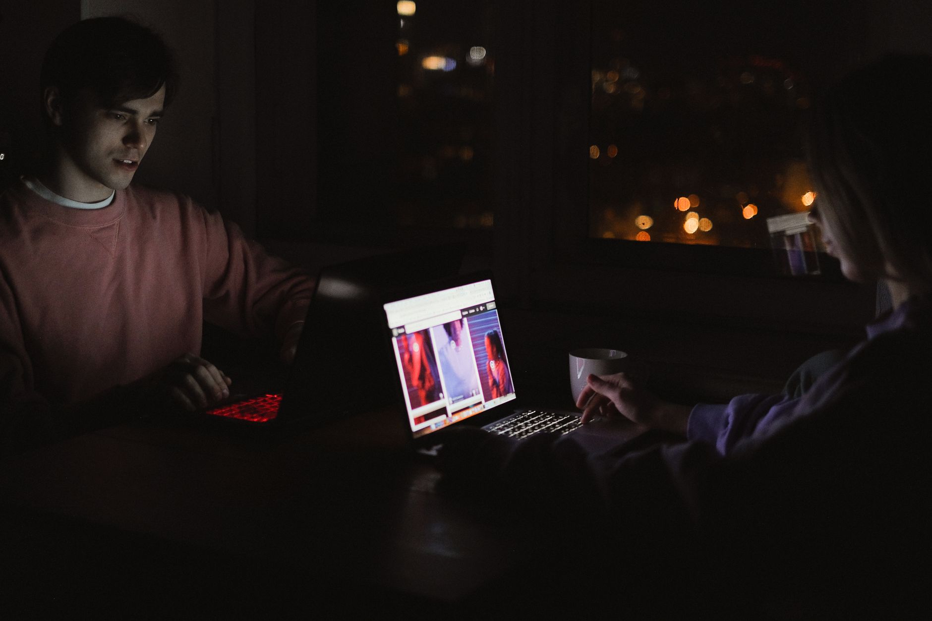 Two people collaborating over laptops in a low-lit workspace.